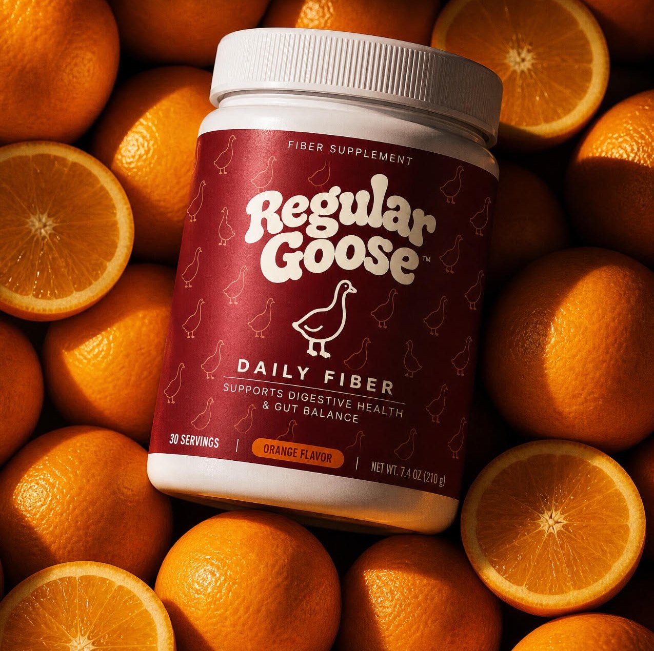A jar of Regular Goose Daily Fiber lit dramatically among whole and halved oranges